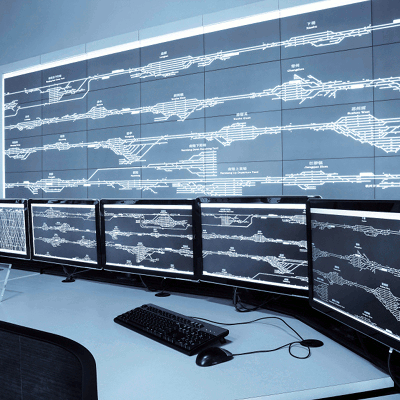 A desk with many monitors in front of a wall of more monitors.The monitors depict a series of tubes.
